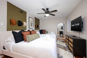 A hotel room with a large bed, a ceiling fan, a TV, and a wall-mounted mirror. - Giddy Up Getaway Pool Hot Tub Family Fun (San Antonio)