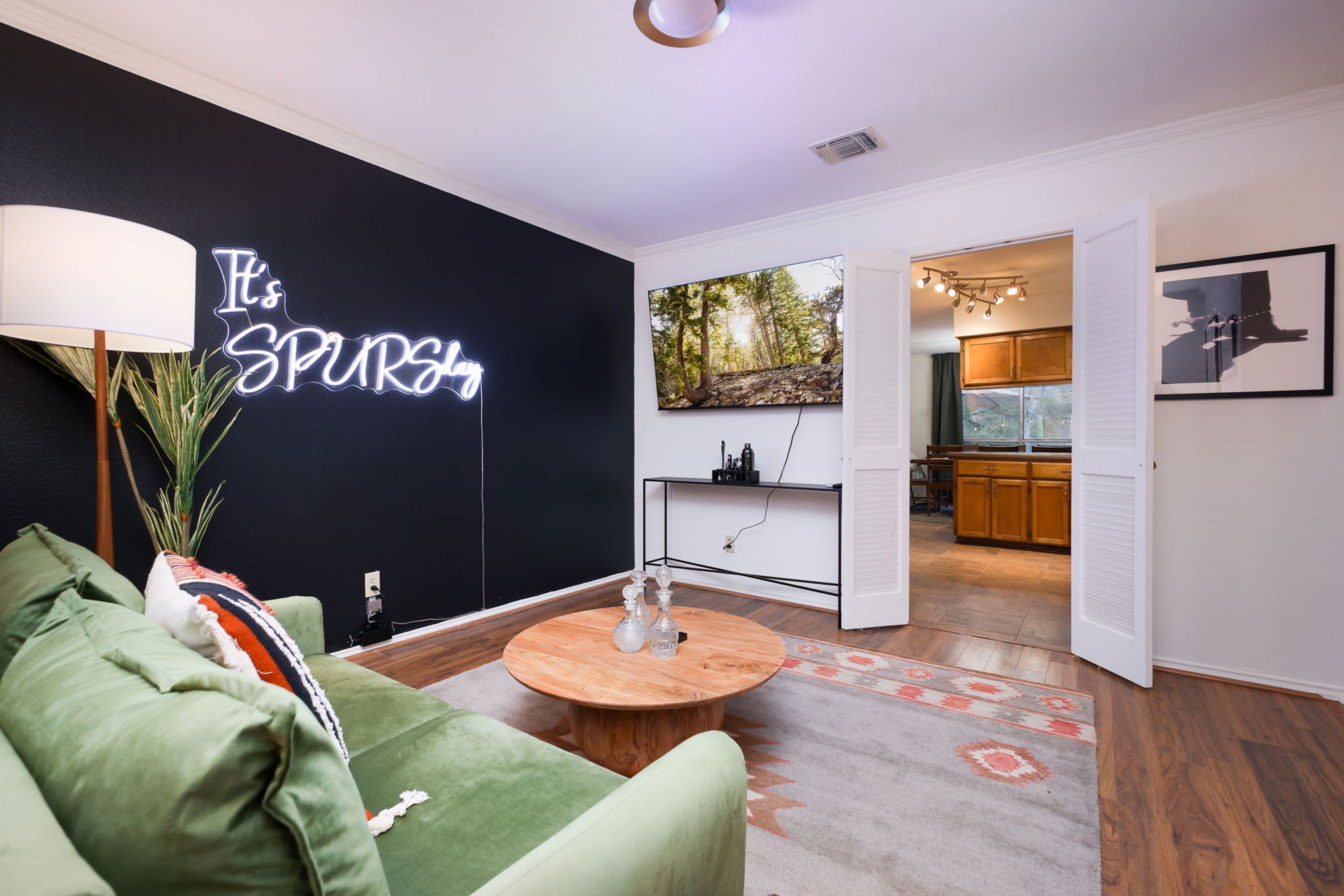 A modern living room with a black wall, a neon sign, a green sofa, a wooden coffee table, and a kitchen in the background.