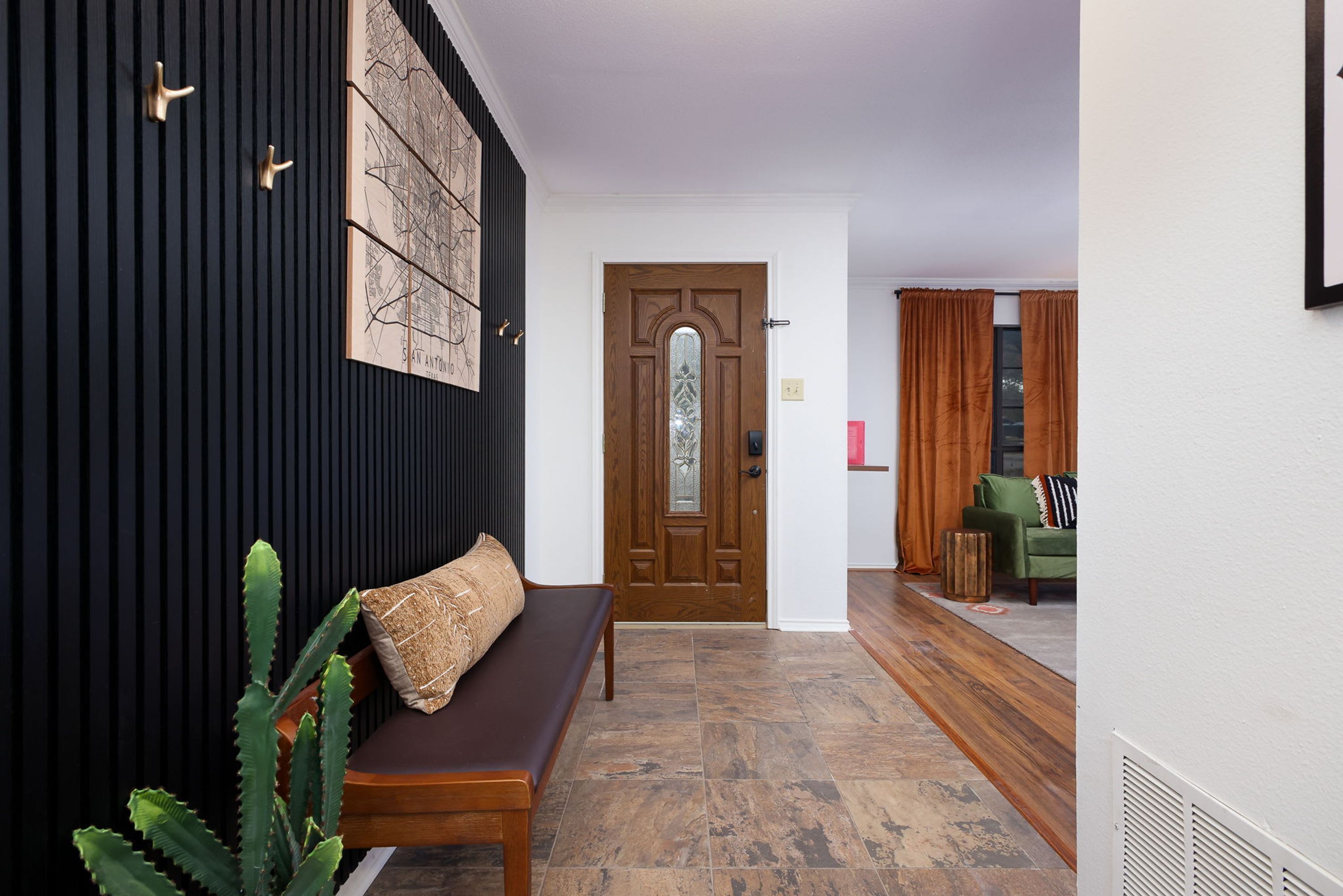 Un pasillo con un banco de madera, una planta de cactus y una puerta con panel de vidrio.