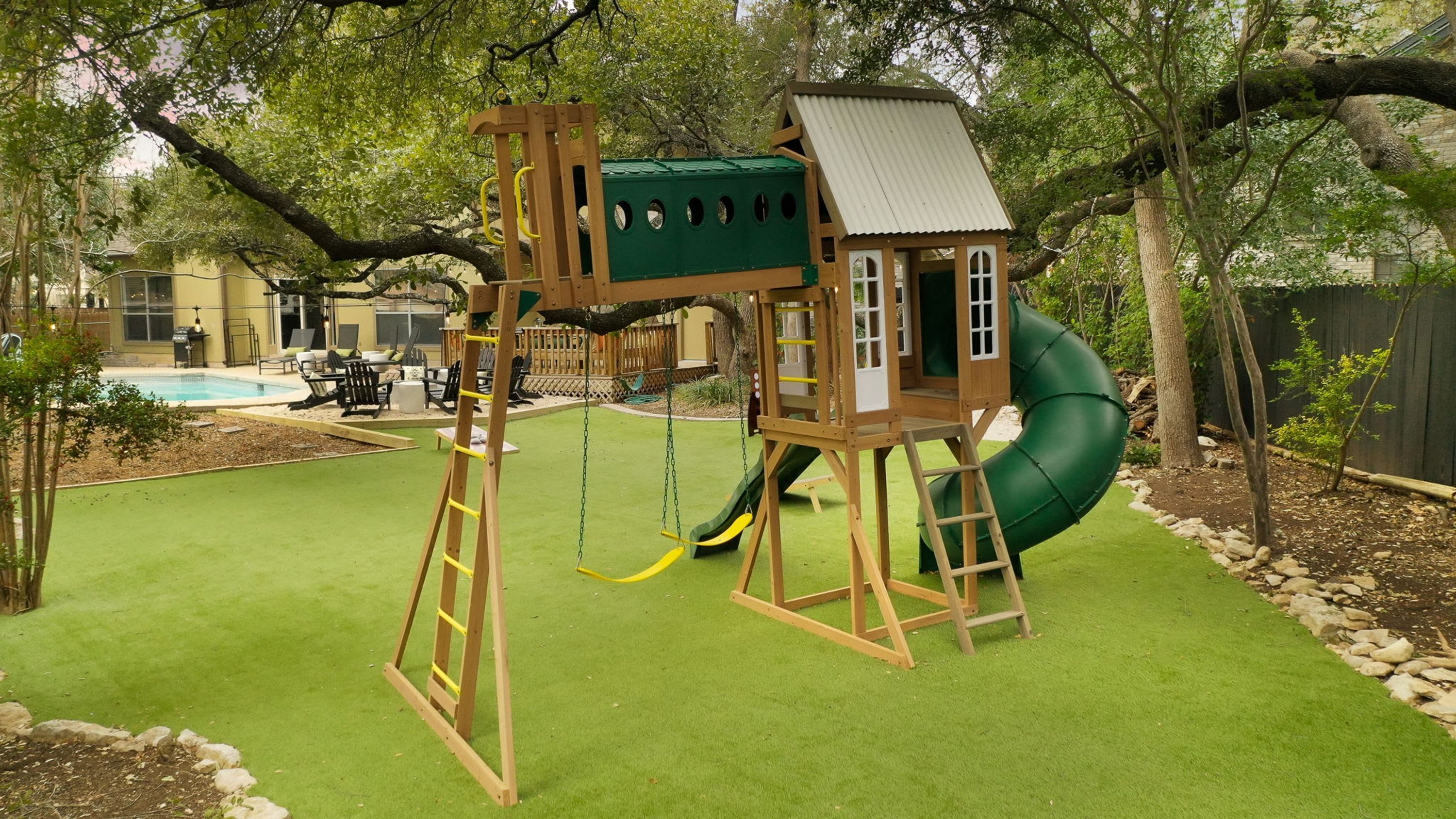 A wooden play structure with a slide and a swing set in a backyard with artificial grass.