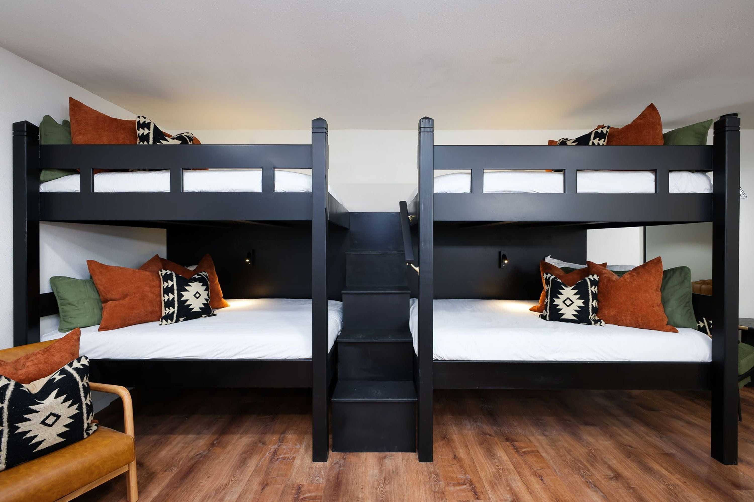 Quarto com beliche, escada central, soalho de madeira e várias almofadas.