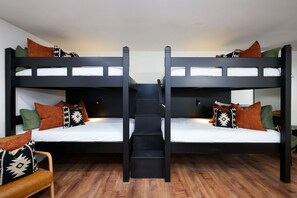 Quarto com beliche, escada central, soalho de madeira e várias almofadas.