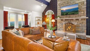 A living room with a stone fireplace, leather sofas, and a large window with curtains. - 14k sq ft Mountaintop Estate - Private Golf Course (Fletcher)