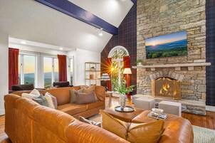 Una sala de estar con chimenea de piedra, sofás de cuero y un ventanal con cortinas.