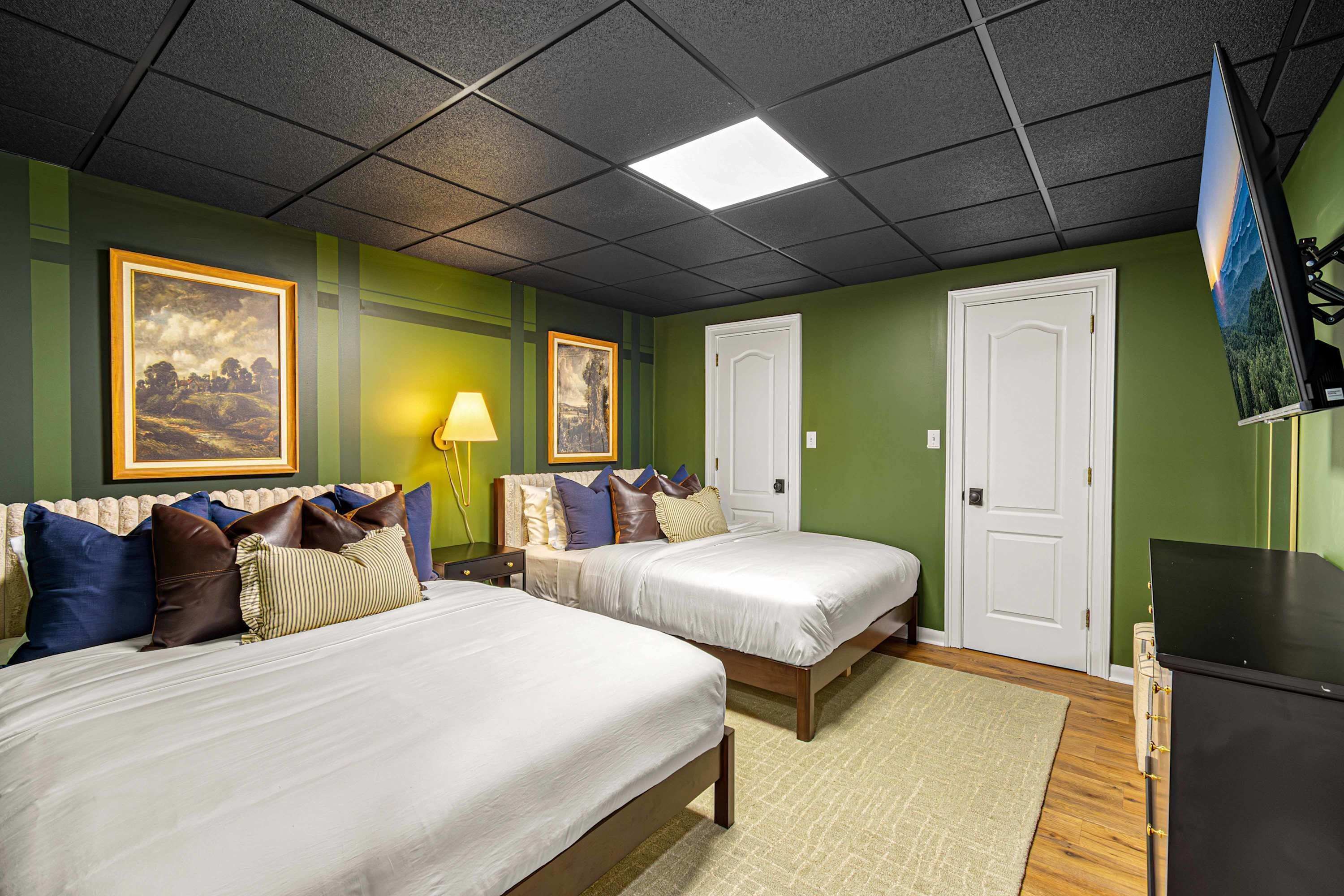 A hotel room with two beds, a desk, a lamp, and artwork on the walls.