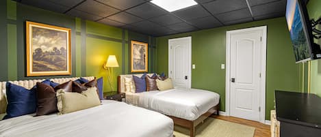 A hotel room with two beds, a desk, a lamp, and artwork on the walls.