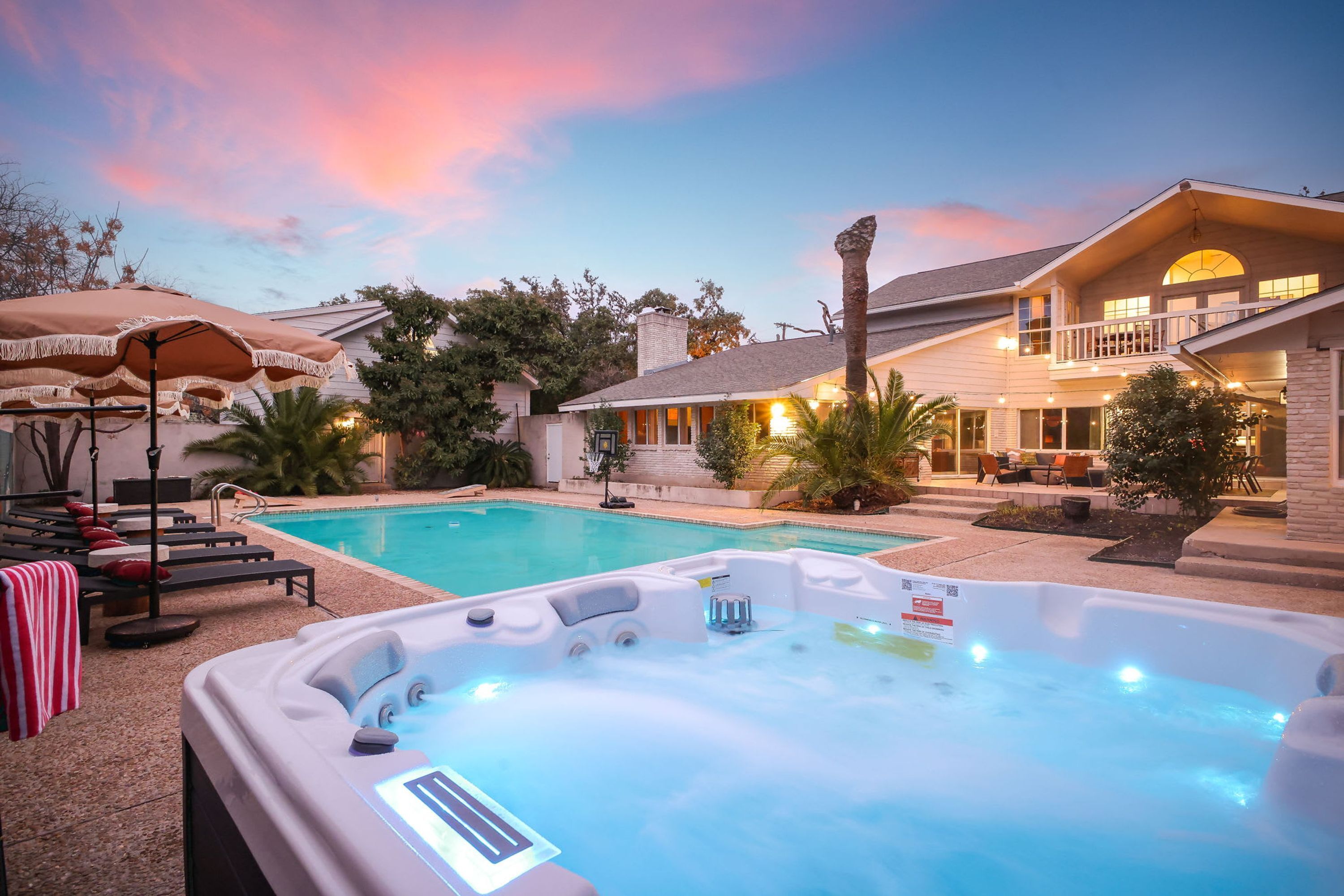 A swimming pool with a hot tub, lounge chairs, and umbrellas.