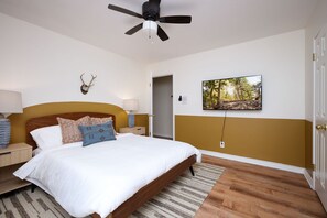 A bedroom with a bed, a ceiling fan, a mounted deer head, a painting, and a door. - Huge Pickleball Mansion Sleeps 26 Pool Hot Tub (San Antonio)