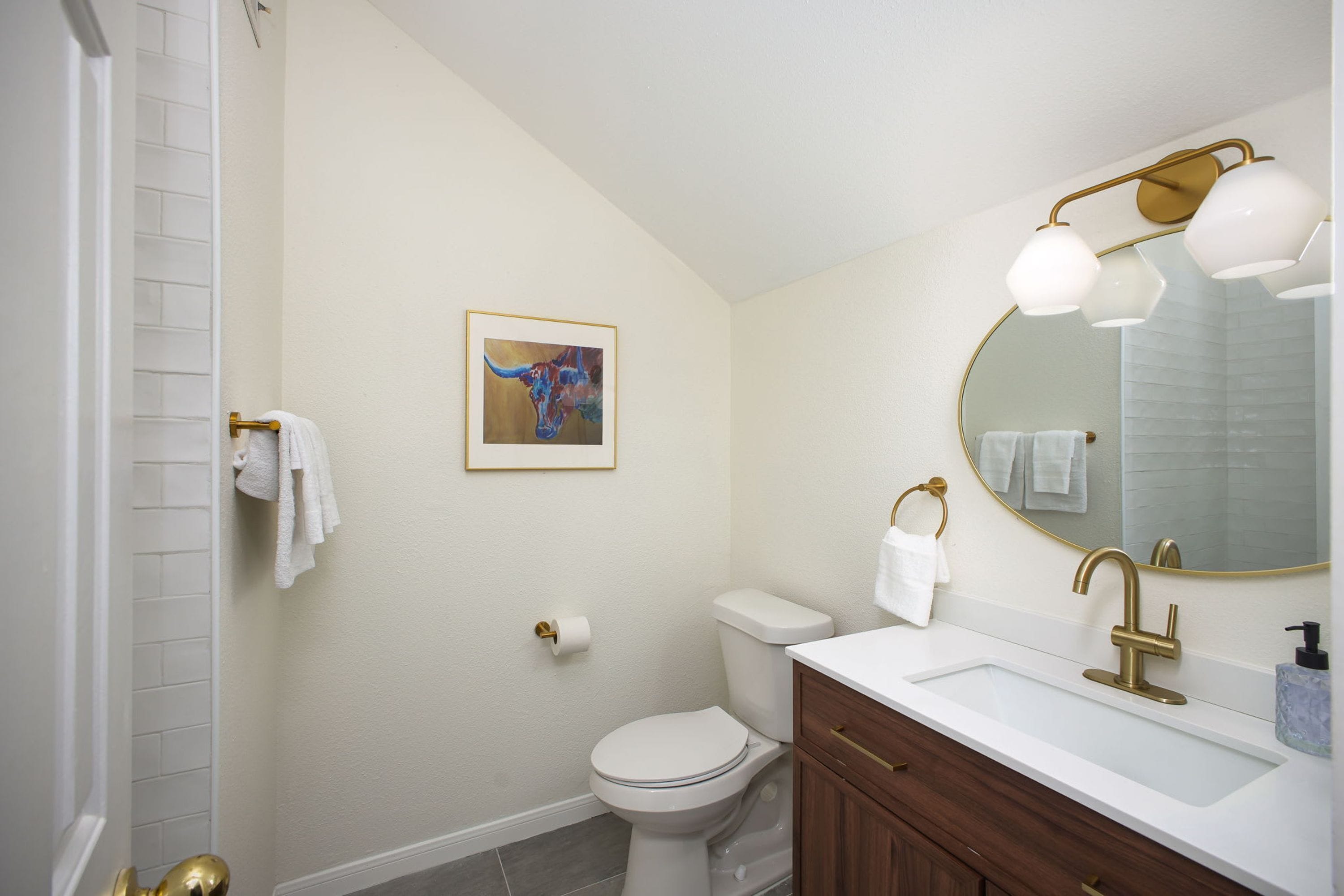 A bathroom with a toilet, sink, and mirror. There is a towel rack and a framed picture on the wall.