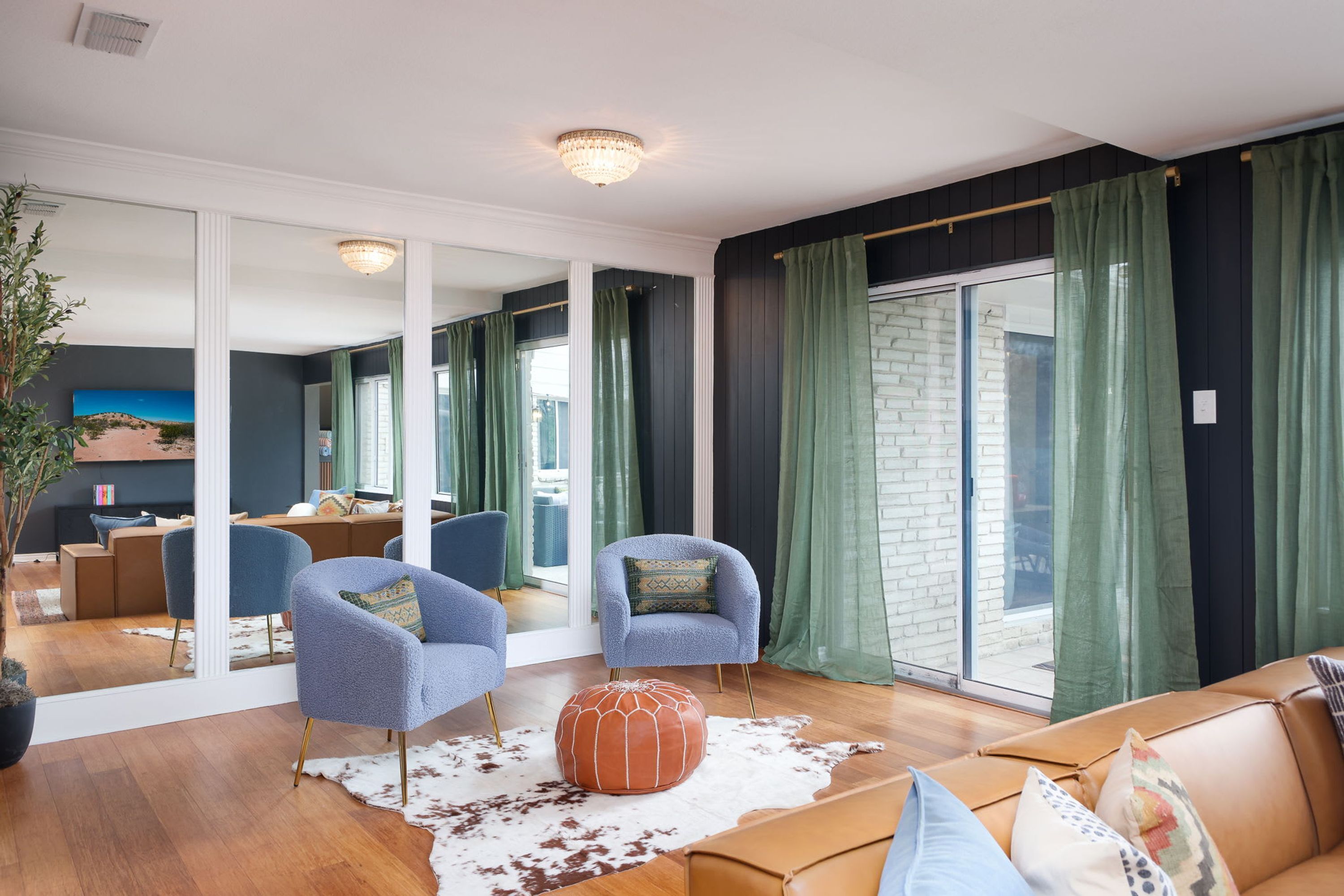 Ein modernes Wohnzimmer mit einem großen Spiegel, zwei Sesseln, einem Sofa und einem Kuhfellteppich.