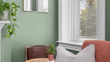A room with a green wall, a window with blinds, a mirror, a brown chair, a red sofa, and a small table with a plant.