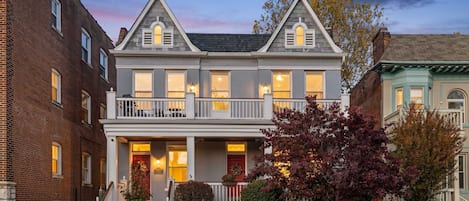 A two-story house with a front porch, a red door, and a brick facade.
