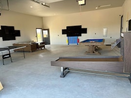 A spacious indoor area with a pool table, a ping pong table, and a seating area with a wicker sofa.