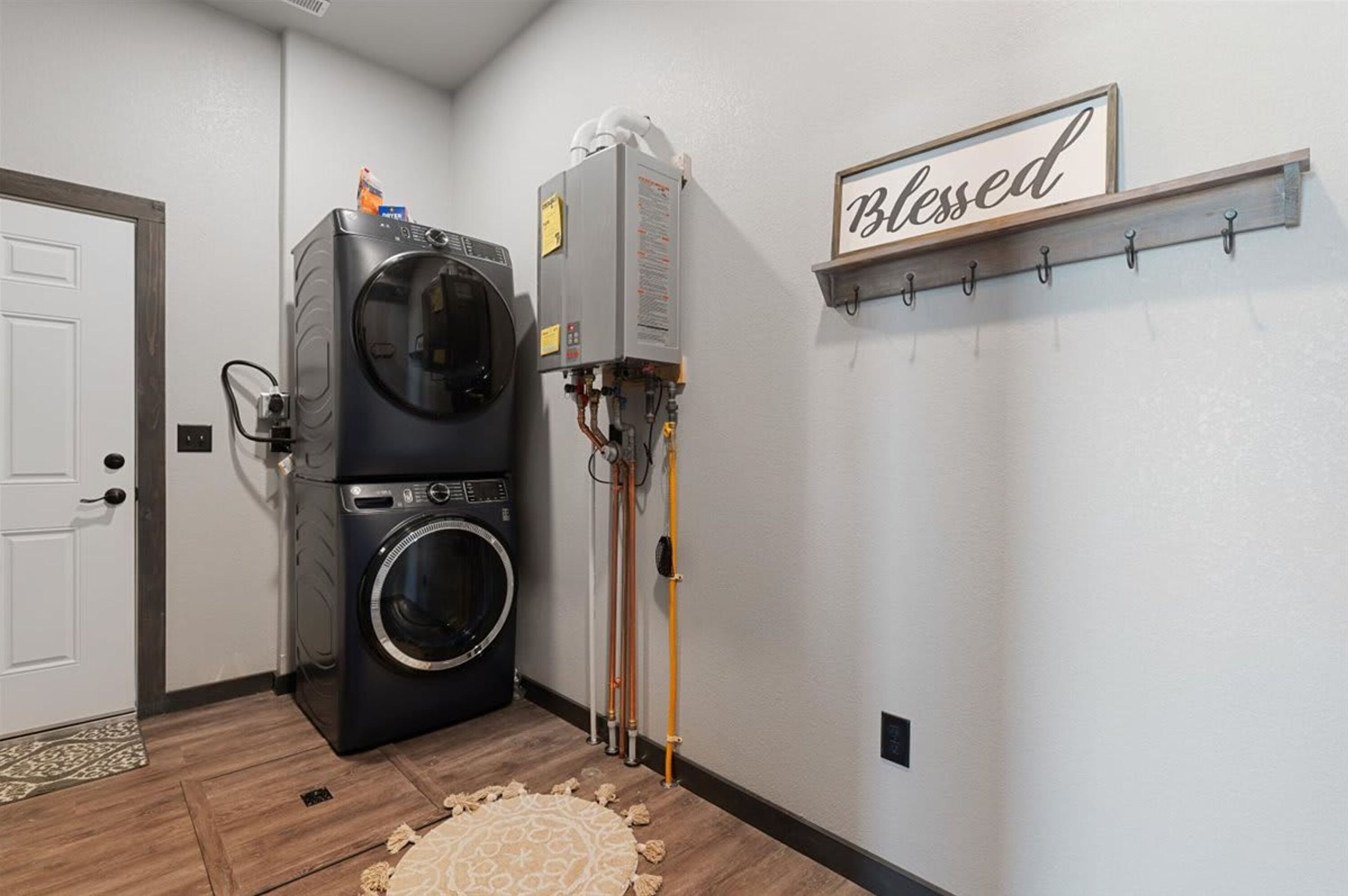 A laundry room with a front-loading washer and dryer, a water heater, and a sign on the wall that reads 'Blessed'.
