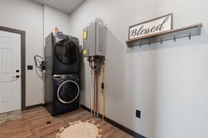 Un lavadero con lavadora y secadora de carga frontal, un calentador de agua y un letrero en la pared que dice 'Blessed'.