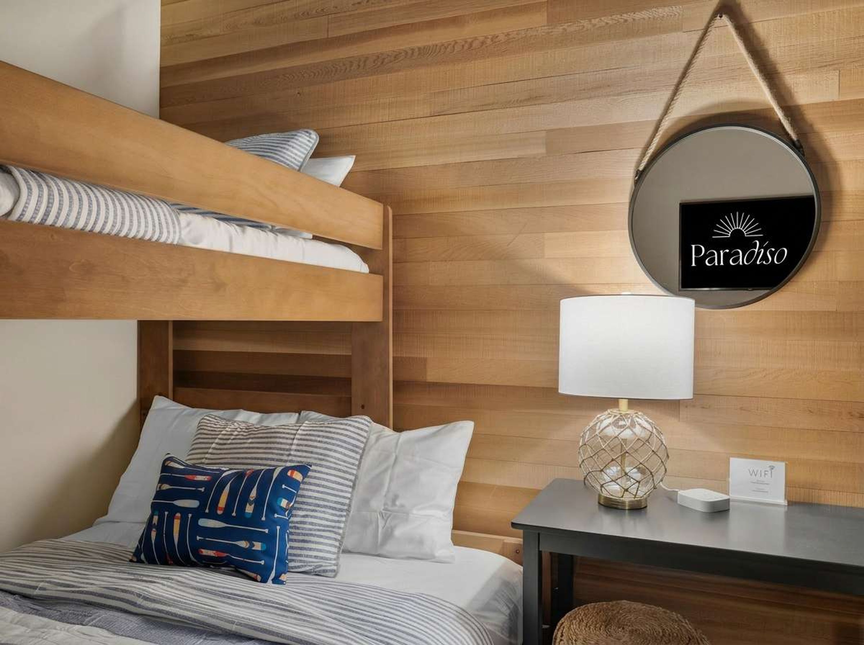 Une chambre d’hôtel avec un lit superposé, une table de chevet avec une lampe et un miroir rond sur lequel est inscrit le mot « Paradiso ».