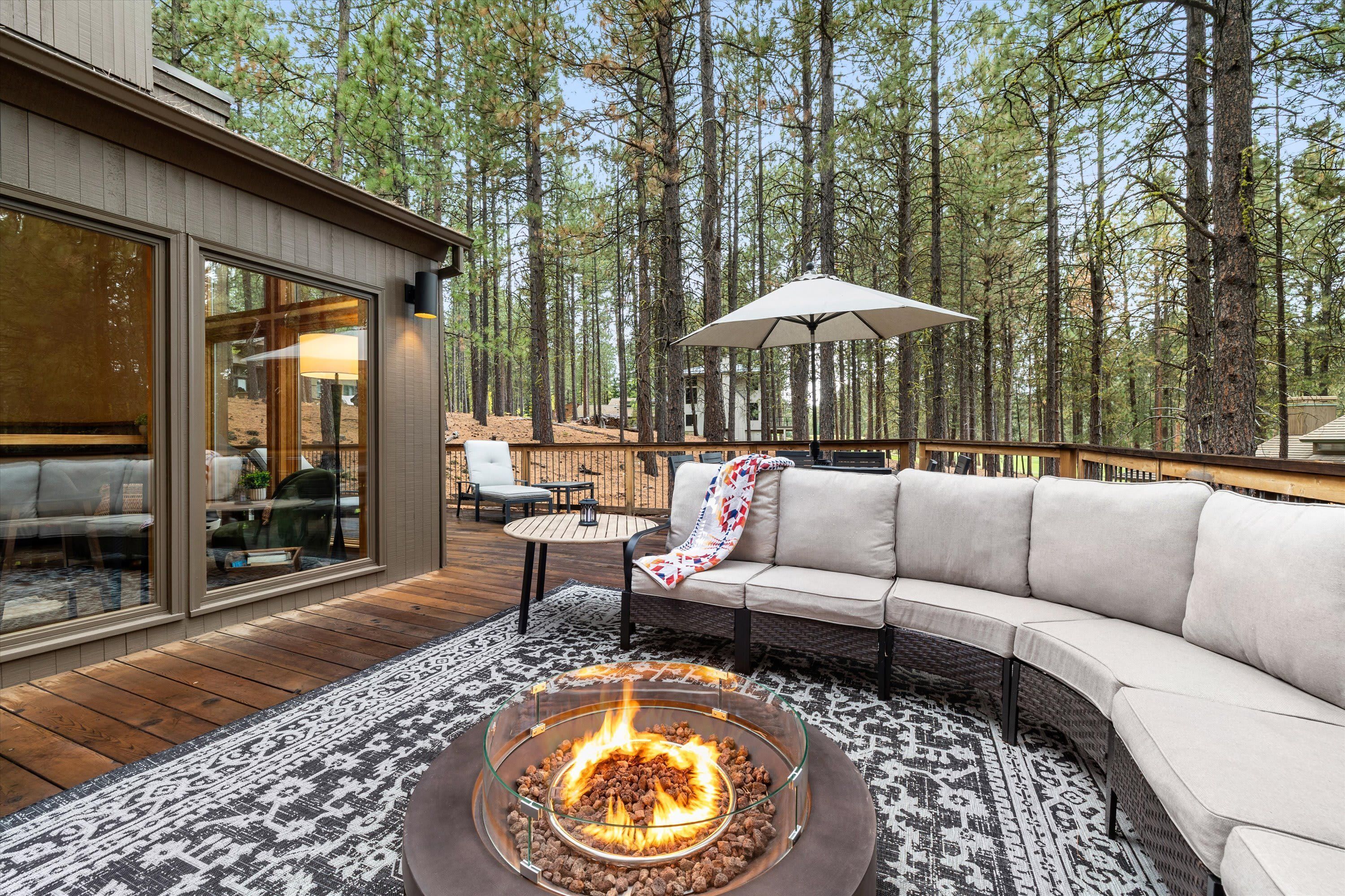 A deck with a fire pit, outdoor furniture, and a view of a forest.