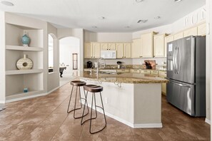 A modern kitchen with a central island, bar stools, a stainless steel refrigerator, and light-colored cabinetry. - HTD Pool Fire Pit Games Dog Friendly Ping Pong (Chandler)