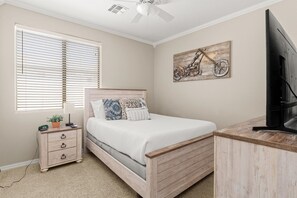 A bedroom with a bed, nightstand, lamp, and a mounted television. - HTD Pool Fire Pit Games Dog Friendly Ping Pong (Chandler)