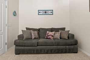 A grey sofa with patterned cushions in a room with a plain wall and a small decorative item above it. - HTD Pool Fire Pit Games Dog Friendly Ping Pong (Chandler)