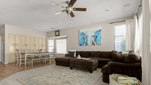 A spacious living room with a sectional sofa, a dining area with a table and chairs, a ceiling fan, and a large abstract painting. - HTD Pool Fire Pit Games Dog Friendly Ping Pong (Chandler)