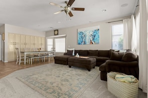 A spacious living room with a sectional sofa, a dining area with a table and chairs, a ceiling fan, and a large abstract painting. - HTD Pool Fire Pit Games Dog Friendly Ping Pong (Chandler)