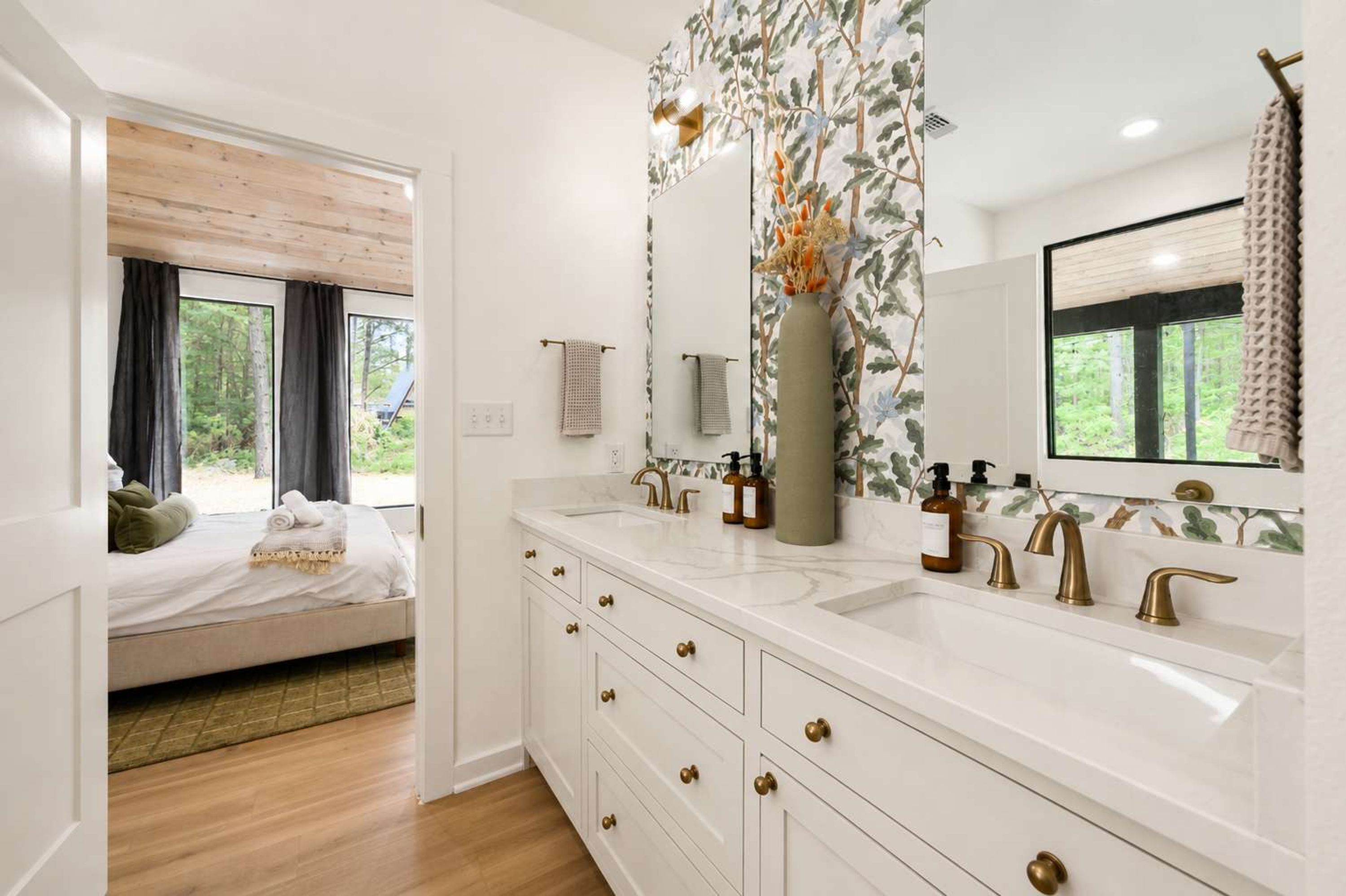 A modern bathroom with a large mirror, two sinks with gold faucets, and a wooden floor.