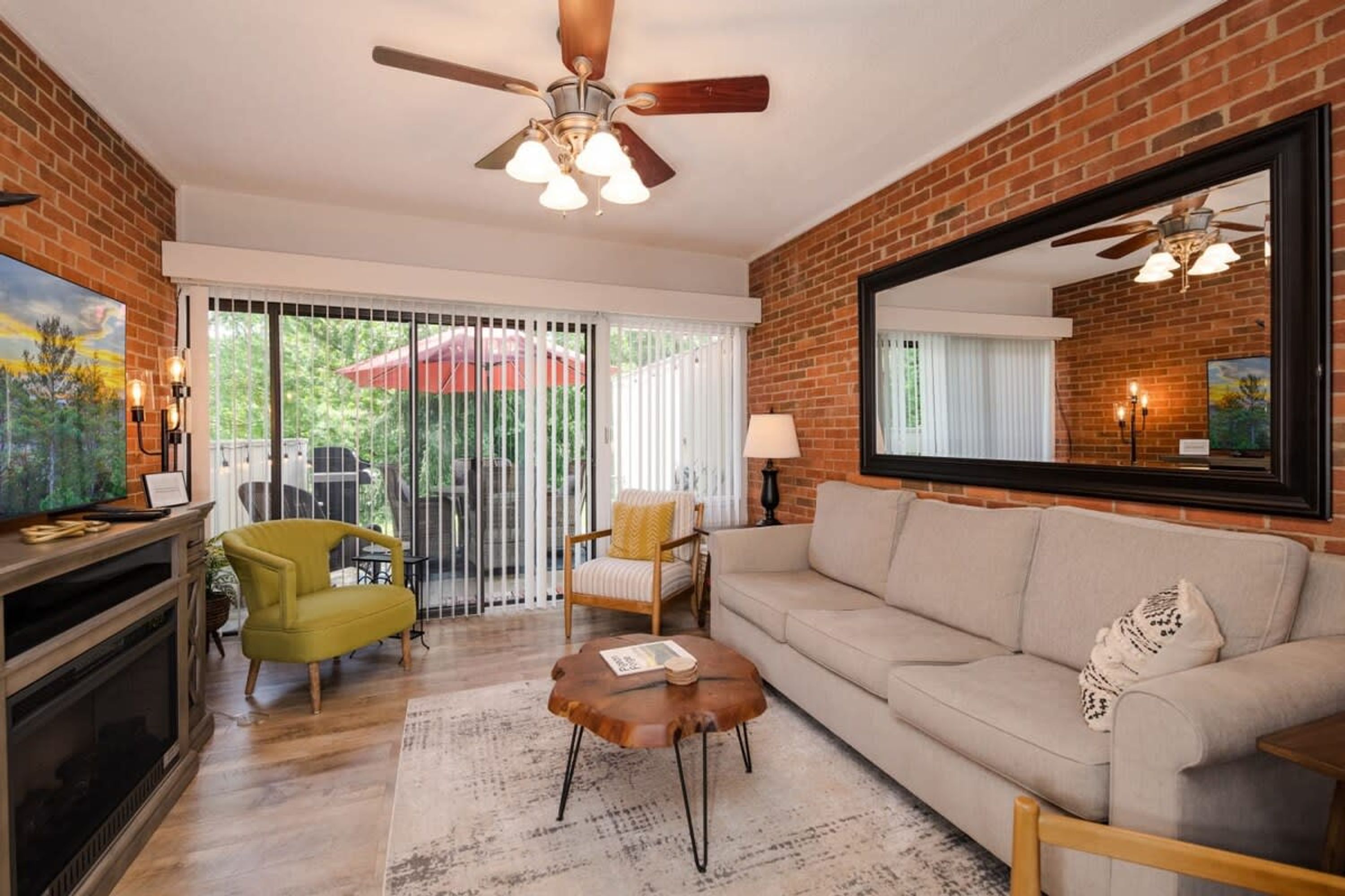 A living room with a brick wall, a ceiling fan, a television, a sofa, a coffee table, and a fireplace.