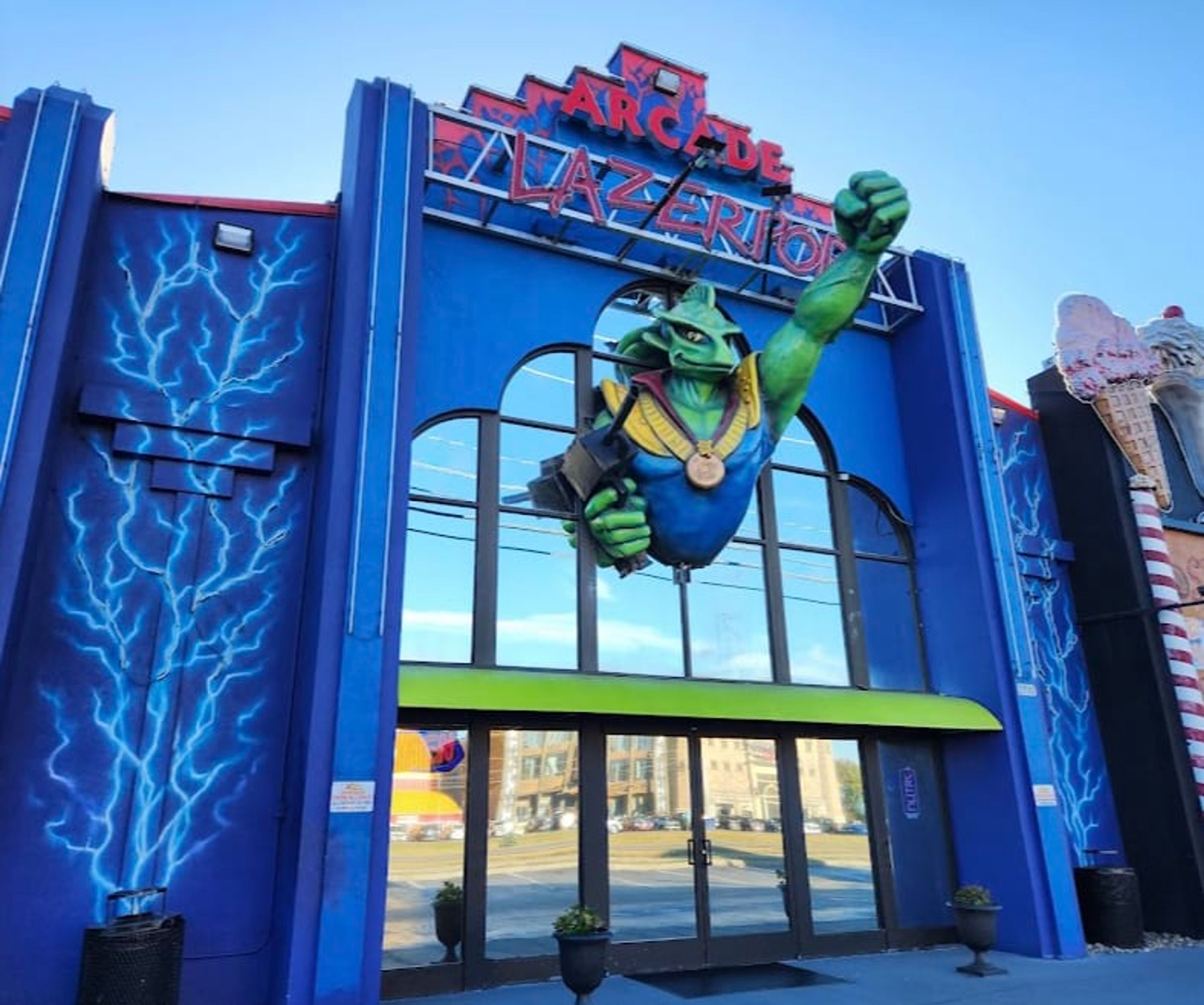 A building entrance with a large green mascot figure and a sign reading 'Arcade'.