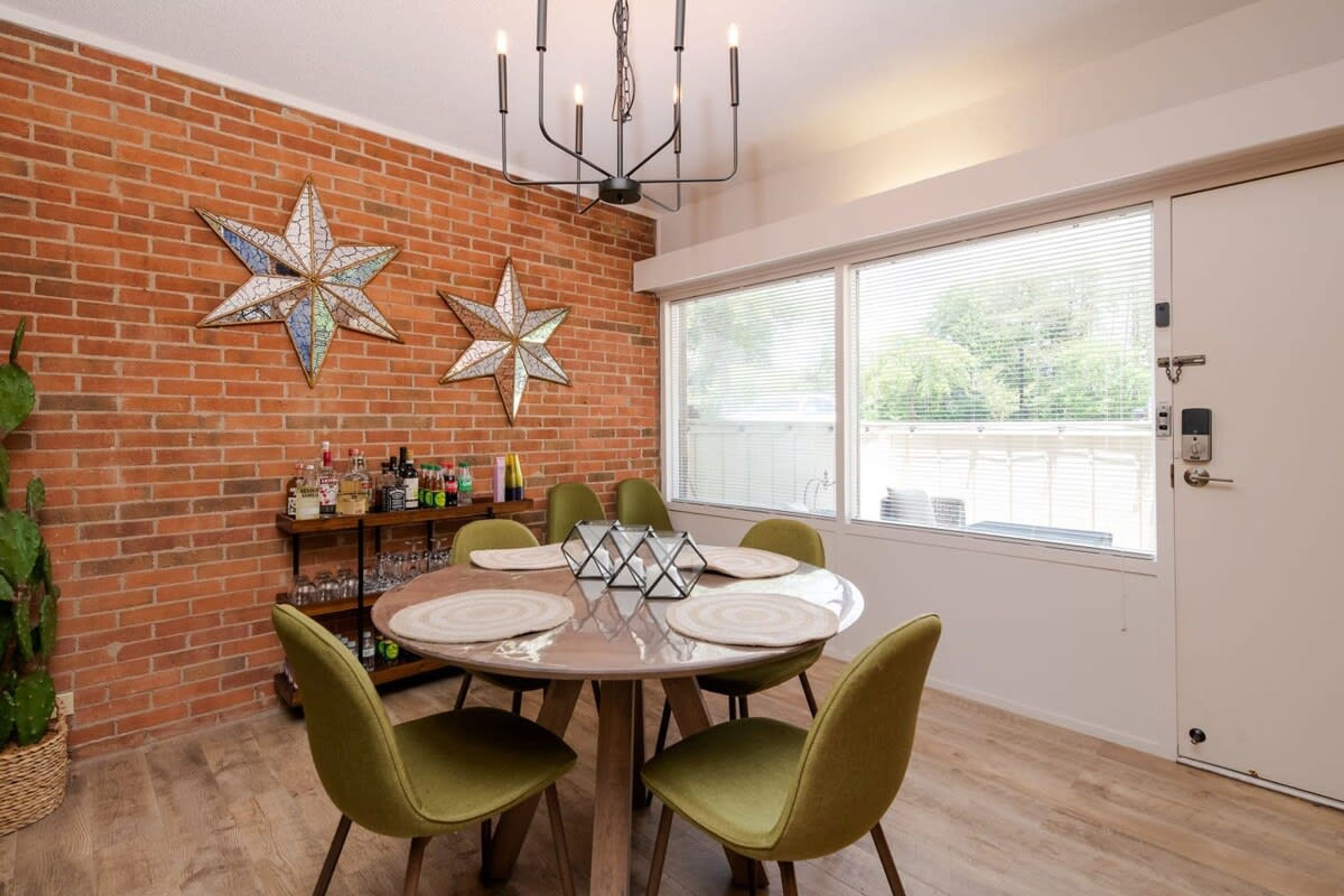 A dining area with a brick wall, star decorations, a chandelier, and a window with blinds.
