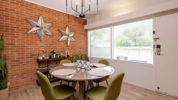 A dining area with a brick wall, star decorations, a chandelier, and a window with blinds.