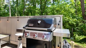 En portabel Spirit-grill med en kontrollpanel, placerad utomhus med utsikt över ett skogsområde.