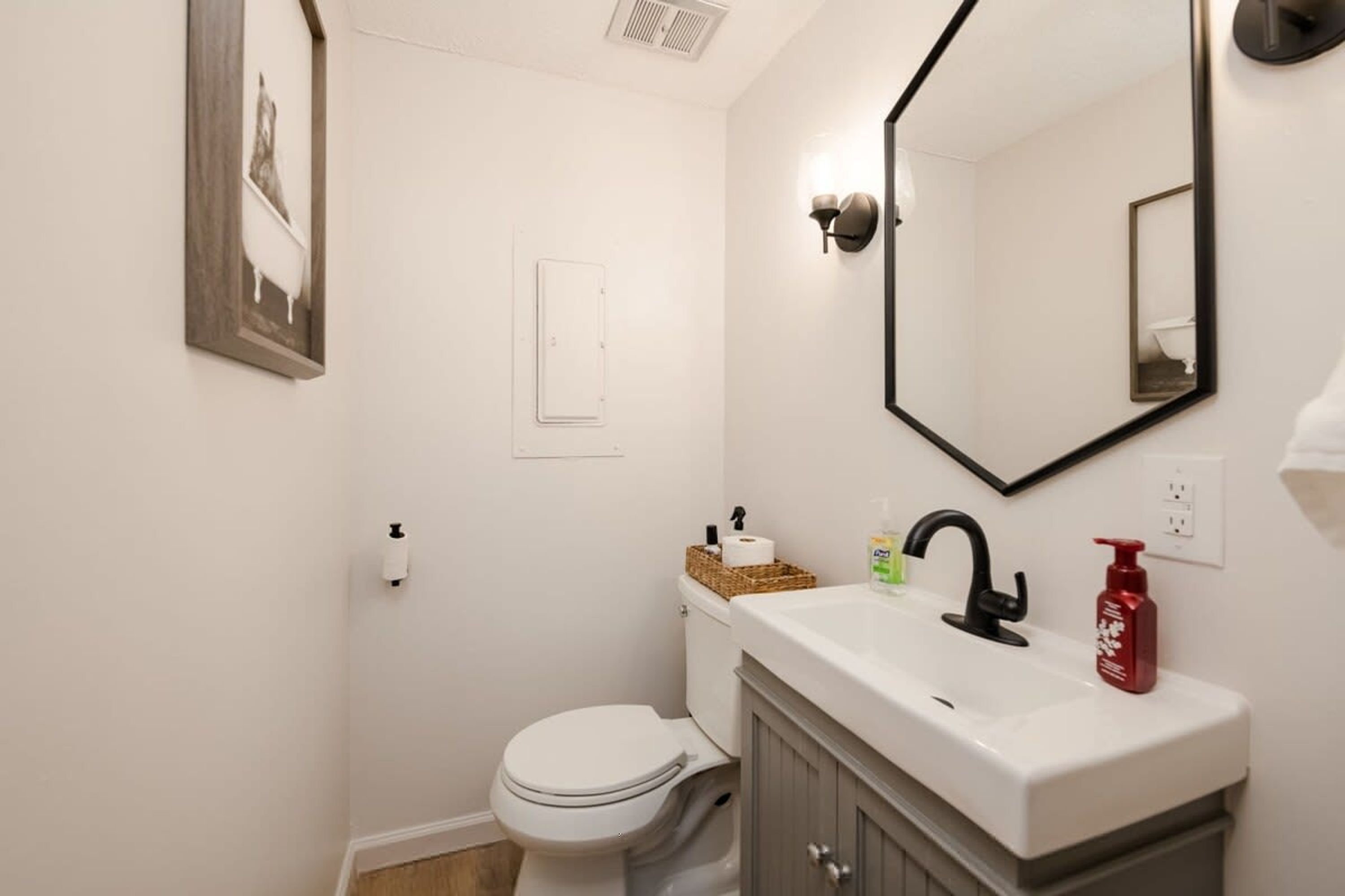 A bathroom with a toilet, sink, mirror, and a framed picture on the wall.