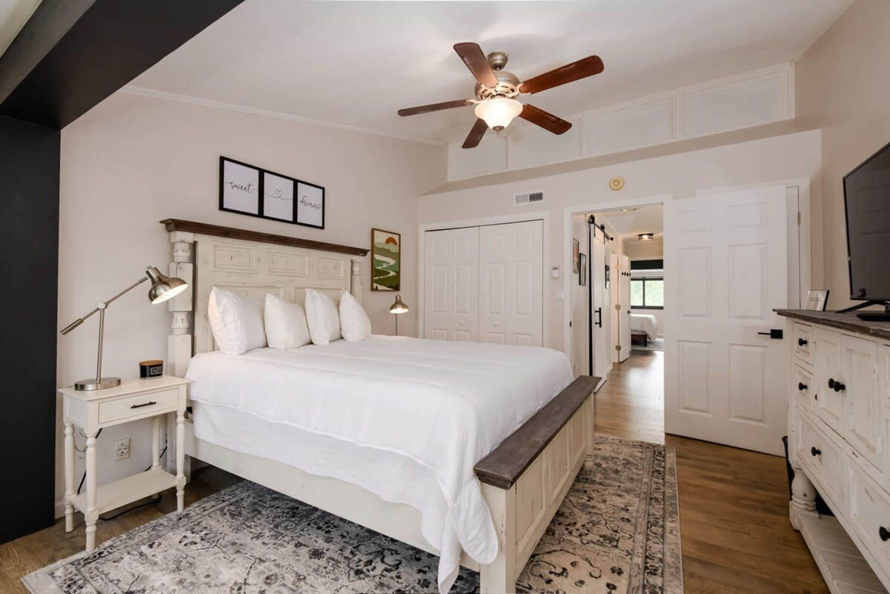 A bedroom with a bed, bedside tables, a ceiling fan, a rug, and a dresser.