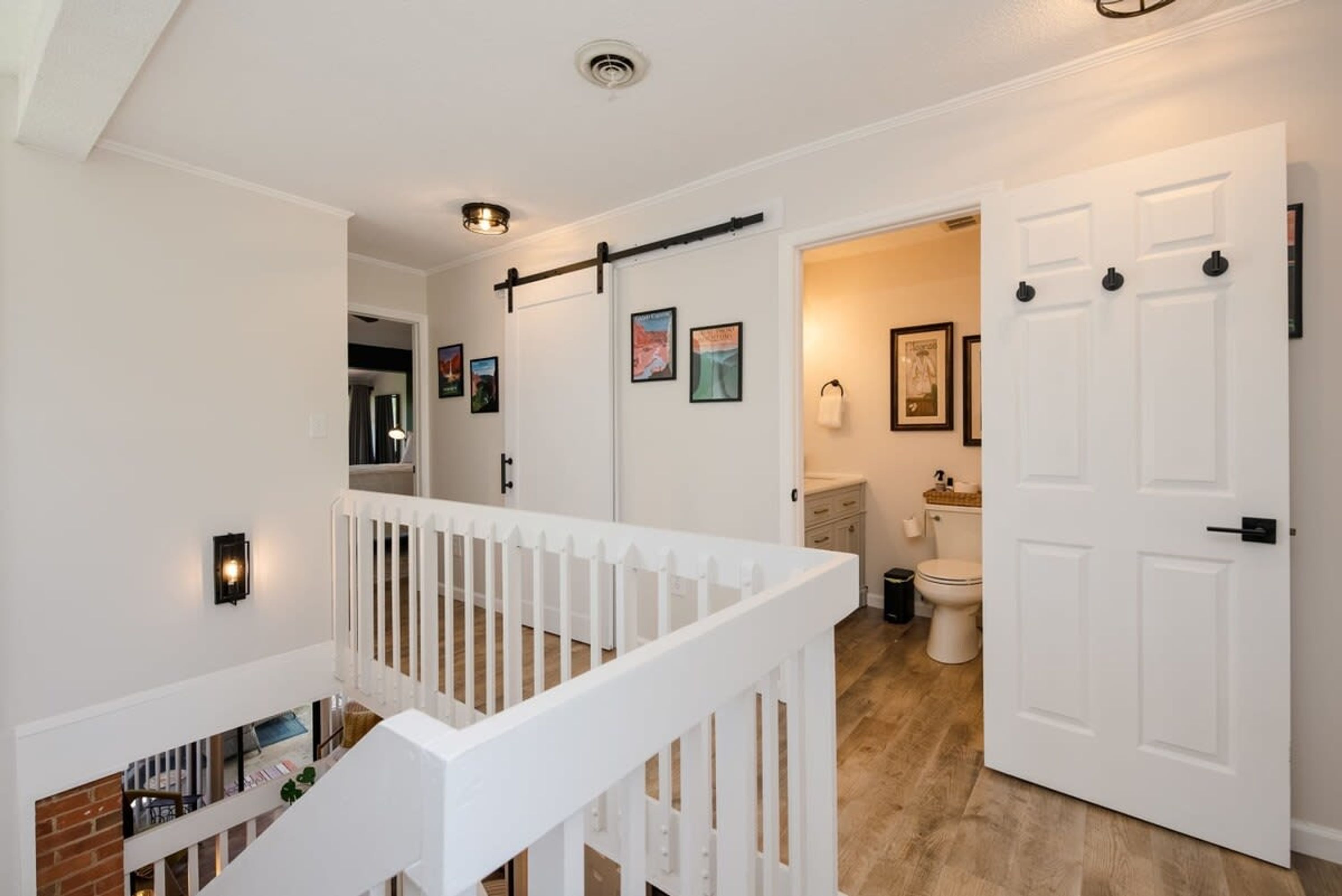 A staircase with a white railing leading to a landing, a white door with a black handle, and a bathroom visible through an open door.