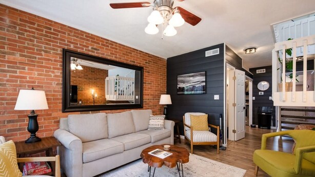 A living room with a brick wall, a ceiling fan, a sofa, a coffee table, and a chair. - Close 2 Dollywood Rustic Sleeps 6 Family Fun (Pigeon Forge)