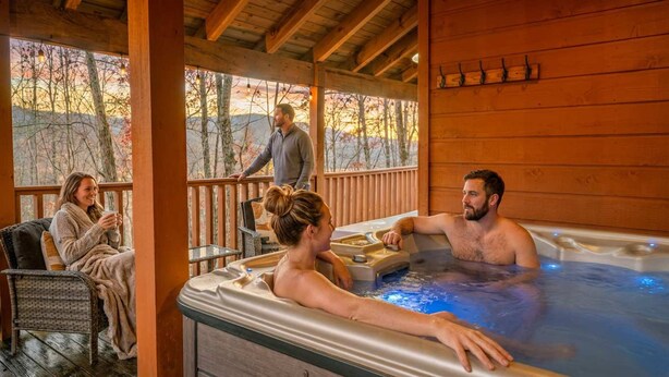 A wooden deck with a hot tub, outdoor seating, and a view of trees. - The Smoky Mountain Sanctuary Gym Sauna (Gatlinburg)