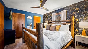 A bedroom with a wooden bed, a ceiling fan, a nightstand, and a wall with floral wallpaper. - The Smoky Mountain Sanctuary Gym Sauna (Gatlinburg)