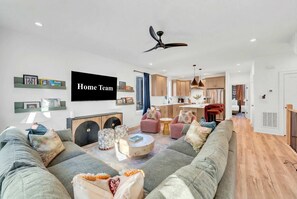 Ein modernes Wohnzimmer mit einer großen Couch, einem Flachbildfernseher und einem Deckenventilator.