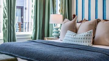 A bed with a blue textured blanket, a patterned pillow, and a bedside lamp.