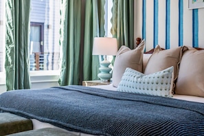 Uma cama com um cobertor azul texturizado, um travesseiro estampado e um abajur.