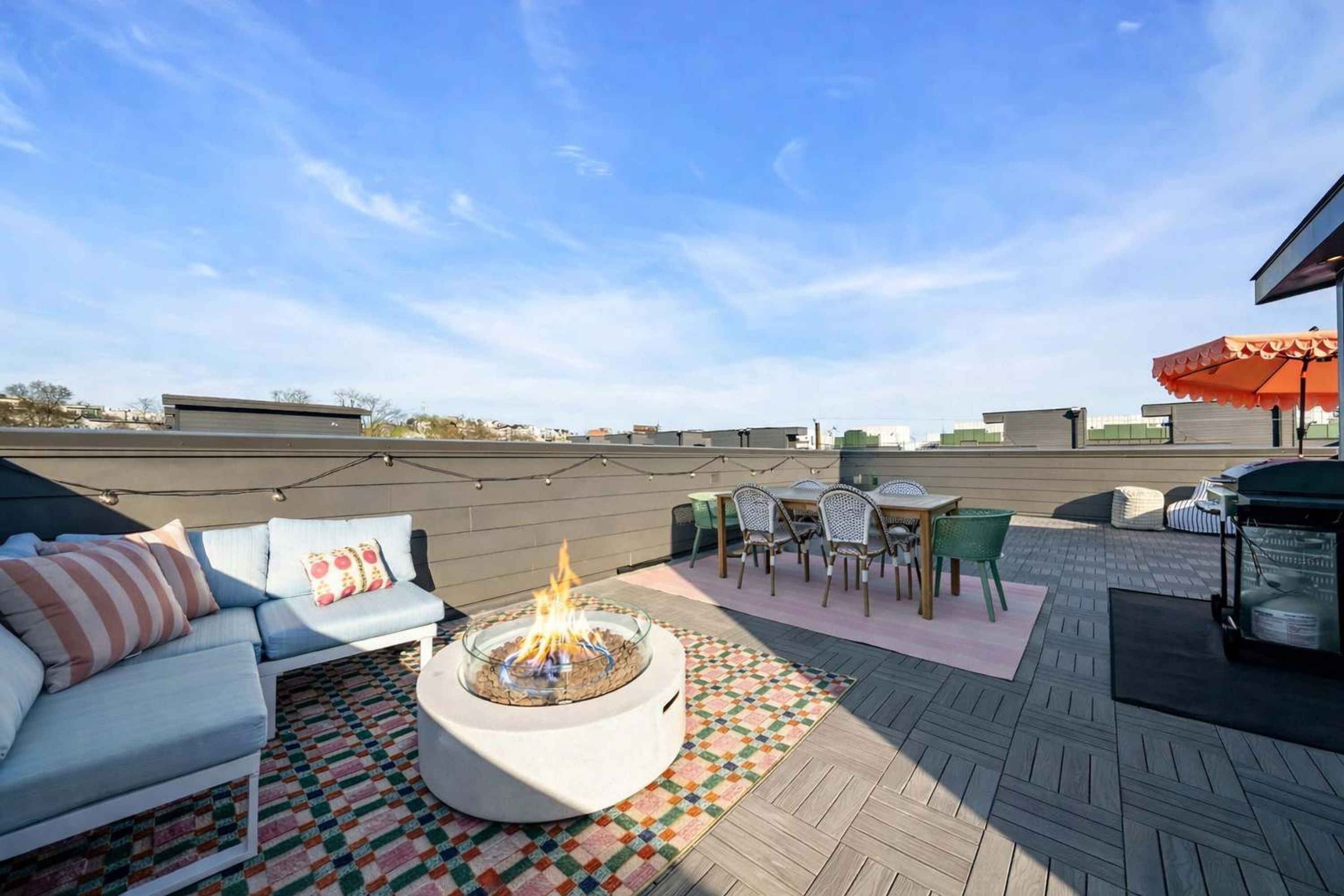A rooftop patio with a fire pit, outdoor furniture, and a view of the city skyline.