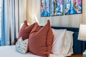 Ein Hotelzimmer mit einem Bett, Kissen, einem Kissen mit Blumenmuster, einem blauen Sofa und einer Wand mit gerahmten Kunstwerken.