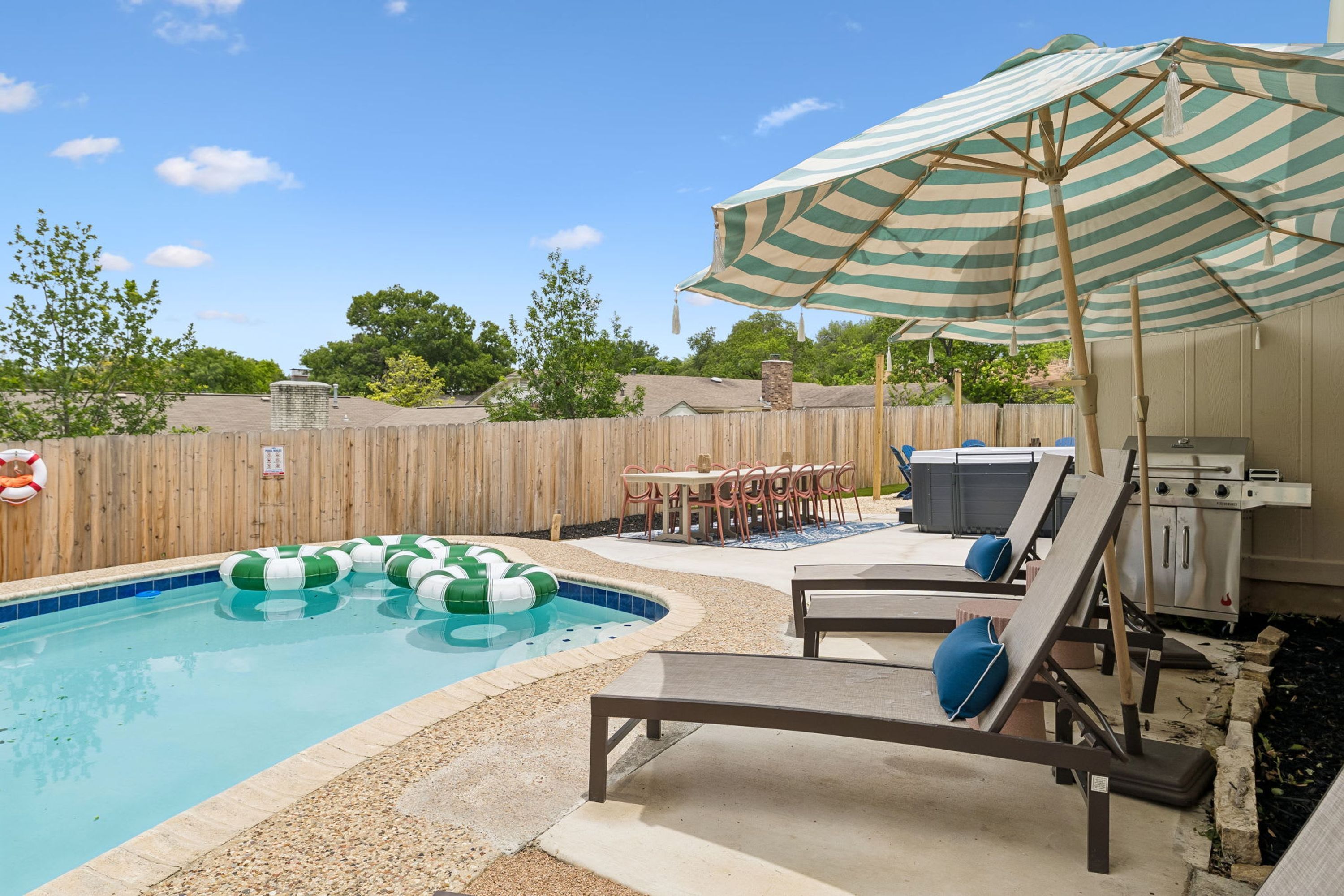 Un cortile con piscina, poltrona da relax, barbecue e recinzione in legno.