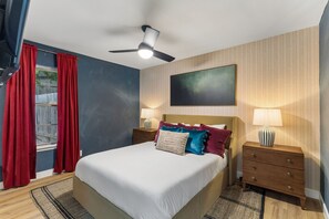 A hotel room with a bed, nightstands, a ceiling fan, a window with curtains, and a wall-mounted artwork. - Cowboy Luxe Retreat Pool Putt Putt Pickleball (San Antonio)