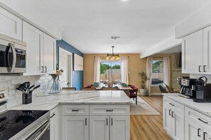 A modern kitchen with white cabinetry, a marble countertop, and a dining area with a view. - Cowboy Luxe Retreat Pool Putt Putt Pickleball (San Antonio)