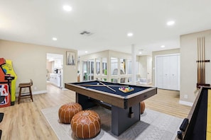 A spacious room with a pool table, ottomans, and a pool cue rack. - Cowboy Luxe Retreat Pool Putt Putt Pickleball (San Antonio)