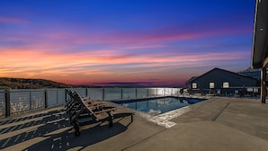 Ein Poolbereich mit einer Bank und Liegestühlen, mit Blick auf ein Gewässer und einen Sonnenuntergang.