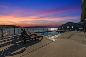 A pool area with a bench and lounge chairs, overlooking a body of water and a sunset. - Sunrise Beach Private Dock Pool (Sunrise Beach)