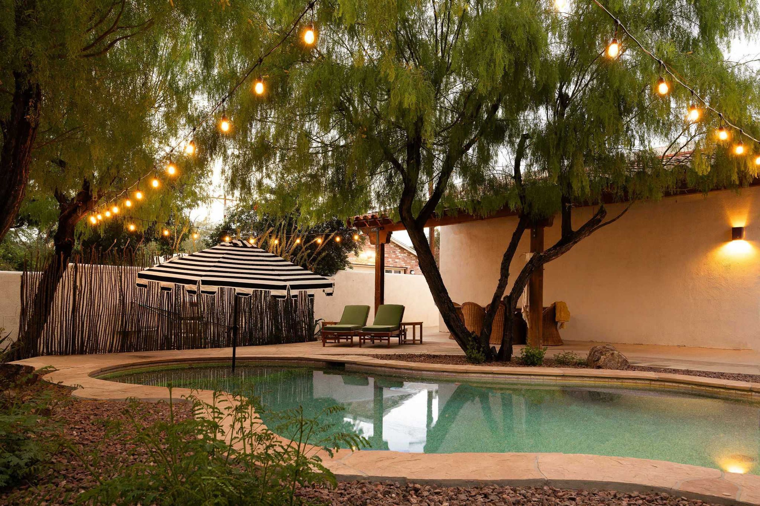 A swimming pool with a surrounding deck, a covered seating area, and string lights.